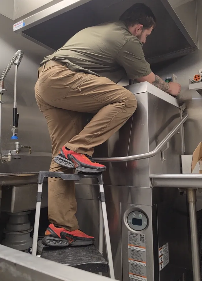 Technician on a ladder servicing a ceiling-mounted commercial unit