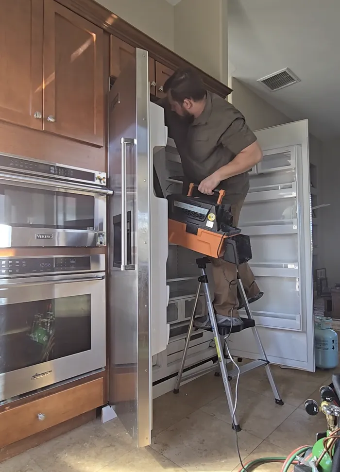 Technician on a ladder servicing a built-in refrigerator